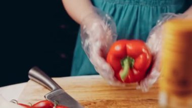 Front view of the young chef cut thin slices of a piece of red pepper with a knife on the cutting board. Front view of a young chef cutting thin slices of a piece of red pepper. Vegetables up close.