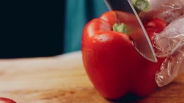 Front view of the young chef cut thin slices of a piece of red pepper with a knife on the cutting board. Front view of a young chef cutting thin slices of a piece of red pepper. Vegetables up close.