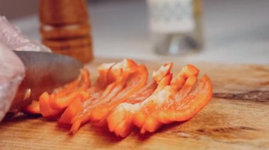 Front view of the young chef cut thin slices of a piece of red pepper with a knife on the cutting board. Front view of a young chef cutting thin slices of a piece of red pepper. Vegetables up close.