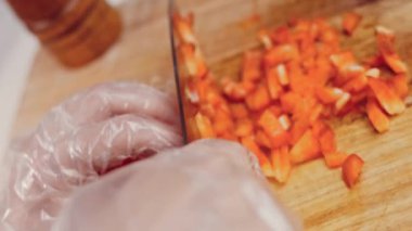 Front view of the young chef cut thin slices of a piece of red pepper with a knife on the cutting board. Front view of a young chef cutting thin slices of a piece of red pepper. Vegetables up close.