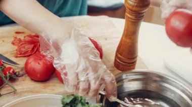 Kırmızı önlüklü şef tencerede domates kesiyor yanındaki masada. Taze sebzelerden yapılan yemek pişirme işlemi, sağlıklı yiyecekler..