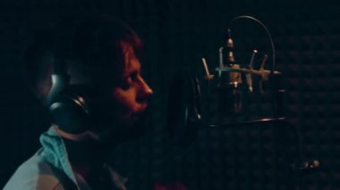 Profesyonel mikrofonlu yakışıklı rap şarkıcısının portresi modern stüdyoda şarkı söylüyor. Müzik prodüksiyonu. Zayıf ışık.
