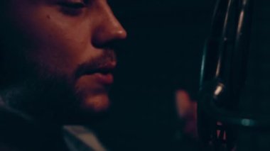 Profesyonel mikrofonlu yakışıklı rap şarkıcısının portresi modern stüdyoda şarkı söylüyor. Müzik prodüksiyonu. Zayıf ışık.