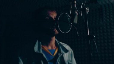 Profesyonel mikrofonlu yakışıklı rap şarkıcısının portresi modern stüdyoda şarkı söylüyor. Müzik prodüksiyonu. Zayıf ışık.