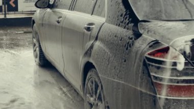 Beyaz köpükle kaplı ve su tabancasından sıçramış lüks araba yıkama işlemi. Parlak araba dış yüzeyine köpük saçılıyor. Güzel bir ortam. 4K video.