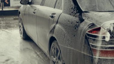 Beyaz köpükle kaplı ve su tabancasından sıçramış lüks araba yıkama işlemi. Parlak araba dış yüzeyine köpük saçılıyor. Güzel bir ortam. 4K video.