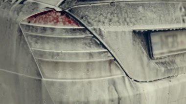 Beyaz köpükle kaplı ve su tabancasından sıçramış lüks araba yıkama işlemi. Parlak araba dış yüzeyine köpük saçılıyor. Güzel bir ortam. 4K video.