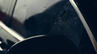 Beyaz köpükle kaplı ve su tabancasından sıçramış lüks araba yıkama işlemi. Parlak araba dış yüzeyine köpük saçılıyor. Güzel bir ortam. 4K video.