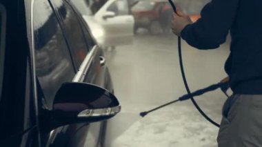 Beyaz köpükle kaplı ve su tabancasından sıçramış lüks araba yıkama işlemi. Parlak araba dış yüzeyine köpük saçılıyor. Güzel bir ortam. 4K video.