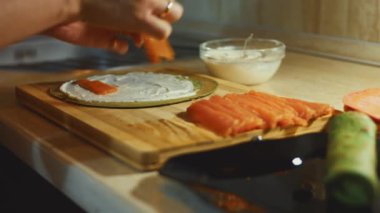 İnce, renkli krepler. Kadınların, somon dilimlerini, ahşap bir tahtanın üzerinde krem peynirle yağlanmış kırmızı krep ile doldurdukları yakın plan. Krepi yuvarlıyorum..