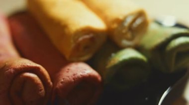 İnce, renkli krepler. Kırmızı, sarı ve yeşil kremalı krem peynirli ve somon balıklı makarna manzaralı bir tabak. 4K video. Yavaş çekim.