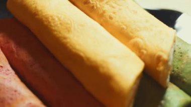 İnce, renkli krepler. Kırmızı, sarı ve yeşil kremalı krem peynirli ve somon balıklı makarna manzaralı bir tabak. 4K video. Yavaş çekim.