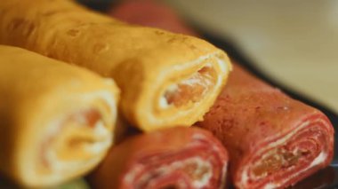 İnce, renkli krepler. Kırmızı, sarı ve yeşil kremalı krem peynirli ve somon balıklı makarna manzaralı bir tabak. 4K video. Yavaş çekim.