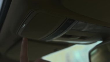 Arabanın içinde ön çatıdaki güneş gözlüğü deposu. Erkek el, güneş gözlüğü deposunu açmak için düğmeye basar. 4K video.