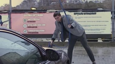 Vitiligo 'su olan genç stil sahibi bir adam oto yıkamada araba temizlemek için yüksek basınçlı jet suyu kullanıyor. 4K video.