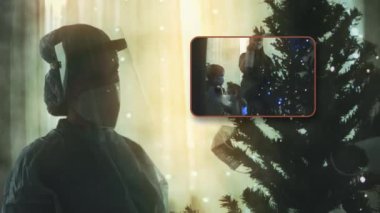 Koruyucu takım elbiseli üzgün doktorun yakın çekimi ve güneşlik Noel ağacını tıbbi maskelerle süslüyor. Sonra da maskeleri çıkarıp süslemelerle dermante ediyor. Noel ve Yeni Yıl Kutlaması