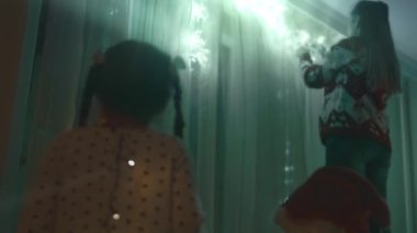 Noel tatili için evlerini dekore eden aile. Güzel mutlu kızlar ışıklarla oynayıp sarılıyorlar. Mutlu Noeller ve mutlu tatiller. Mutlu aile zamanları..