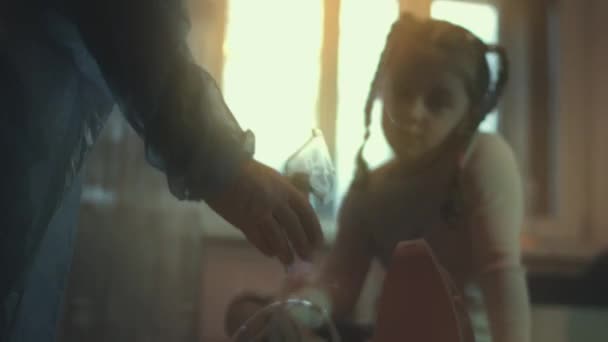 漂亮的小女孩坐在沙发上 用压缩机吸入器吸气 女孩吸入盐水蒸气 脸上戴着雾化面罩 妈妈帮助女儿吸气 — 图库视频影像