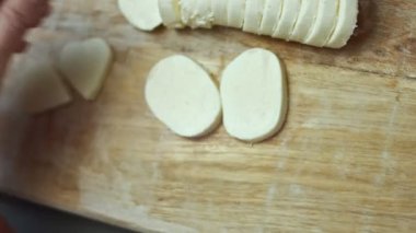 Ahşap kesme tahtasının üzerinde kalp şeklinde mozzarella peyniri kesen kadın elleri. Sevgililer Günü için yemek hazırlıyorum. 4K video. Sanatsal çekim.