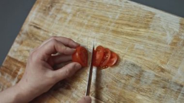 Tahtada mutfak bıçağıyla kırmızı kiraz domateslerini dilimlemek, sevgililer günü için kalp şeklinde pizza hazırlamak. 4K video.