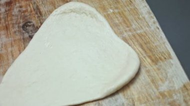 Tahta kesme tahtasının üzerinde pizza için taze hamur hazırlıyorum. Sevgililer Günü için kalp şeklinde pizza hazırlıyorum. Sevdiğim biri için. 4K video. Sanatsal çekim.