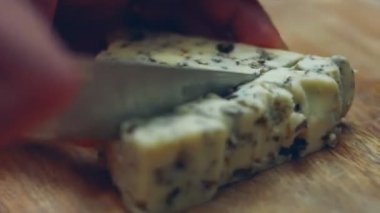 Danimarka mavi peyniri. Mycella peyniri kesme tahtasının arka planında bir kadın eliyle açıldı. 4K video. Sanatsal çekim, yavaş çekim.