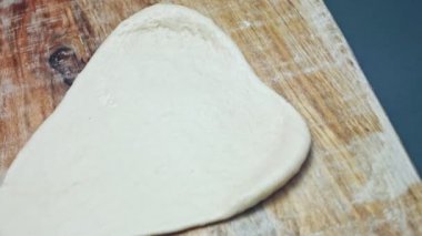 Tahta kesme tahtasının üzerinde pizza için taze hamur hazırlıyorum. Sevgililer Günü için kalp şeklinde pizza hazırlıyorum. Sevdiğim biri için. 4K video. Sanatsal çekim.