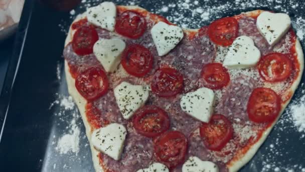 ベーキングトレイにバジルで味付けピザ 愛する人のためのバレンタインデーのためのハート型のピザを準備します 4Kビデオ — ストック動画