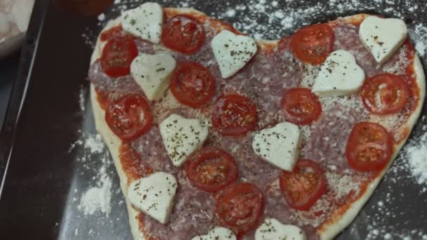 ベーキングトレイ上のハート型のピザにスライスしたチェリートマトを追加します 愛する人のためのバレンタインデーのためのハート型のピザを準備します 4Kビデオ 芸術的射撃 — ストック動画