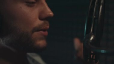 Profesyonel mikrofonlu yakışıklı rap şarkıcısının portresi modern stüdyoda şarkı söylüyor. Müzik prodüksiyonu. Zayıf ışık.