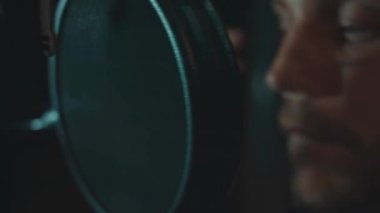 Profesyonel mikrofonlu yakışıklı rap şarkıcısının portresi modern stüdyoda şarkı söylüyor. Müzik prodüksiyonu. Zayıf ışık.