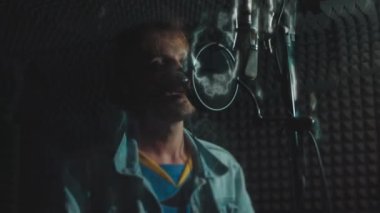 Profesyonel mikrofonlu yakışıklı rap şarkıcısının portresi modern stüdyoda şarkı söylüyor. Müzik prodüksiyonu. Zayıf ışık.
