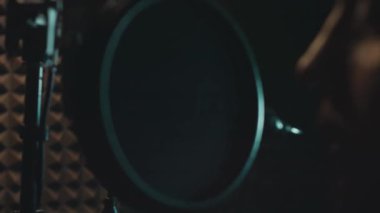 Profesyonel mikrofonlu yakışıklı rap şarkıcısının portresi modern stüdyoda şarkı söylüyor. Müzik prodüksiyonu. Zayıf ışık.