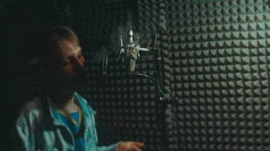 Profesyonel mikrofonlu yakışıklı rap şarkıcısının portresi modern stüdyoda şarkı söylüyor. Müzik prodüksiyonu. Zayıf ışık.