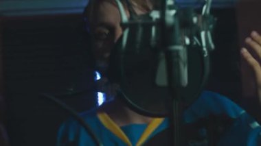 Profesyonel mikrofonlu yakışıklı rap şarkıcısının portresi modern stüdyoda şarkı söylüyor. Müzik prodüksiyonu. Zayıf ışık.