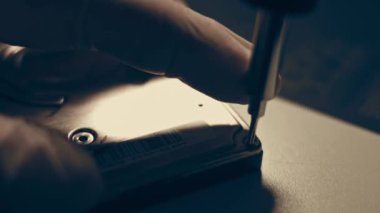 Yakın plan. Tornavida, bilgisayarın sabit diskindeki vidayı söküyor. Erkek eller bilgisayar sabit diskindeki vidayı tornavidayla büker. Bilgisayar sabit diskini onarma ustasının elleri HDD.