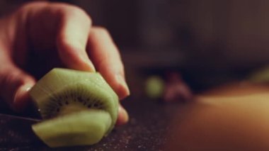 Siyah mermer kesme tahtasında sulu yeşil bir kivi dilimliyorum. Makro görünüm.
