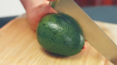 Siyah eldivenli bir şef ahşap bir masada avokado soyar ve keser.