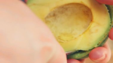 Siyah eldivenli bir şef ahşap bir masada avokado soyar ve keser.