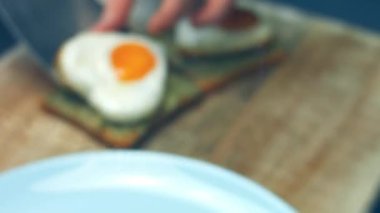 Kırık avokado ve ahşap bir tahtanın üzerinde parmesanlı peynirli tost ekmeği üzerinde kalp şeklinde yumurtalar. 8 Mart 'ta sürpriz kahvaltı hazırlıyorum. Makro görünüm, yavaş çekim