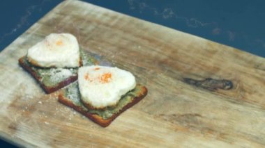 Kırık avokado ve ahşap bir tahtanın üzerinde parmesanlı peynirli tost ekmeği üzerinde kalp şeklinde yumurtalar. 8 Mart 'ta sürpriz kahvaltı hazırlıyorum. Makro görünüm, yavaş çekim