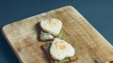 Kırık avokado ve ahşap bir tahtanın üzerinde parmesanlı peynirli tost ekmeği üzerinde kalp şeklinde yumurtalar. 8 Mart 'ta sürpriz kahvaltı hazırlıyorum. Makro görünüm, yavaş çekim