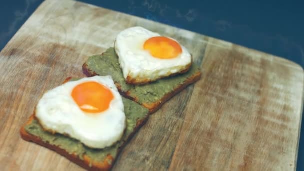 烤面包上有心形的鸡蛋 上面有碎鳄梨和木地板上的半乳酪 为三月八号做一个惊喜早餐 宏观视图 慢动作 — 图库视频影像