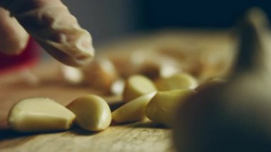 Video kaydı. Genç bir adam manuel sarımsak ezici ile sarımsak eziyor. Peynir, tereyağı, mutfak aletleri masanın üstünde. Evin içi, tatil aydınlatması. Ev mutfağında lezzetli yemekler pişirmek..