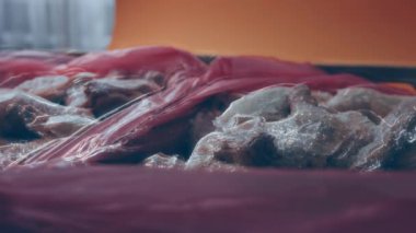 Eldivenli ellerin yakın plan görüntüsü tavuk bacağını bir kutudan ayrı plastik poşetlere paketliyor. Evde daha fazla kullanılmak üzere dondurulmuş etin süreci. Işık oynatma ile 4k video