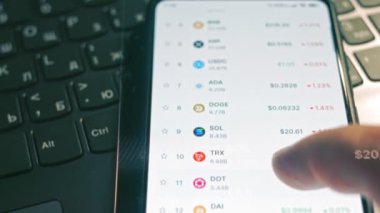 Yatırımcı cep telefonu ekranında Bitcoin, Ethereum ve diğer altsikke kripto para fiyat indeksini kontrol ediyor. Hologram etkisi