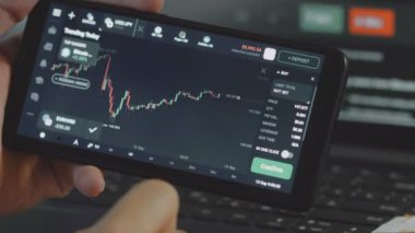 Cep telefonu ekranında kripto para piyasası ve döviz kuru analiz ediliyor. Histogram büyüme ve fiyat endeksinde azalma gösteriyor. Yatırım kavramı