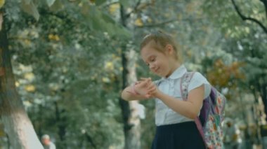 Güzel beyaz liseli kız dersleri bitirdikten sonra okul parkında akıllı çocuk kullanıyor. Mutlu çocuk, akıllı telefondan ailesiyle görüntülü konuşma yapıyor. GPS izleyicili akıllı kol saati
