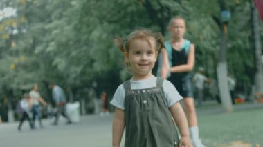 Kafkasya 'nın 2 yıllık güzel portresi. Parkta durup kameraya gülümseyen, iki örgülü saçlı küçük kız.