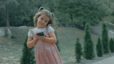 Anaokulunda akıllı telefonuyla oynayan sevimli bir kız. Sağlıklı 5 yıl. Kız cep telefonuna parmaklarıyla dokunuyor, çizgi film izliyor ve eğitim uygulamalarıyla eğleniyor. Dışarıda parkta bir çocuk